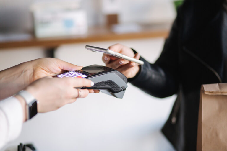 Closeup of female paying with smartphone during Covid-19 pandemic. Cashier hand holding credit card reader machine while client holding phone for NFC payment. View from inside.